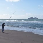 man in black shirt fishing on beach during daytime