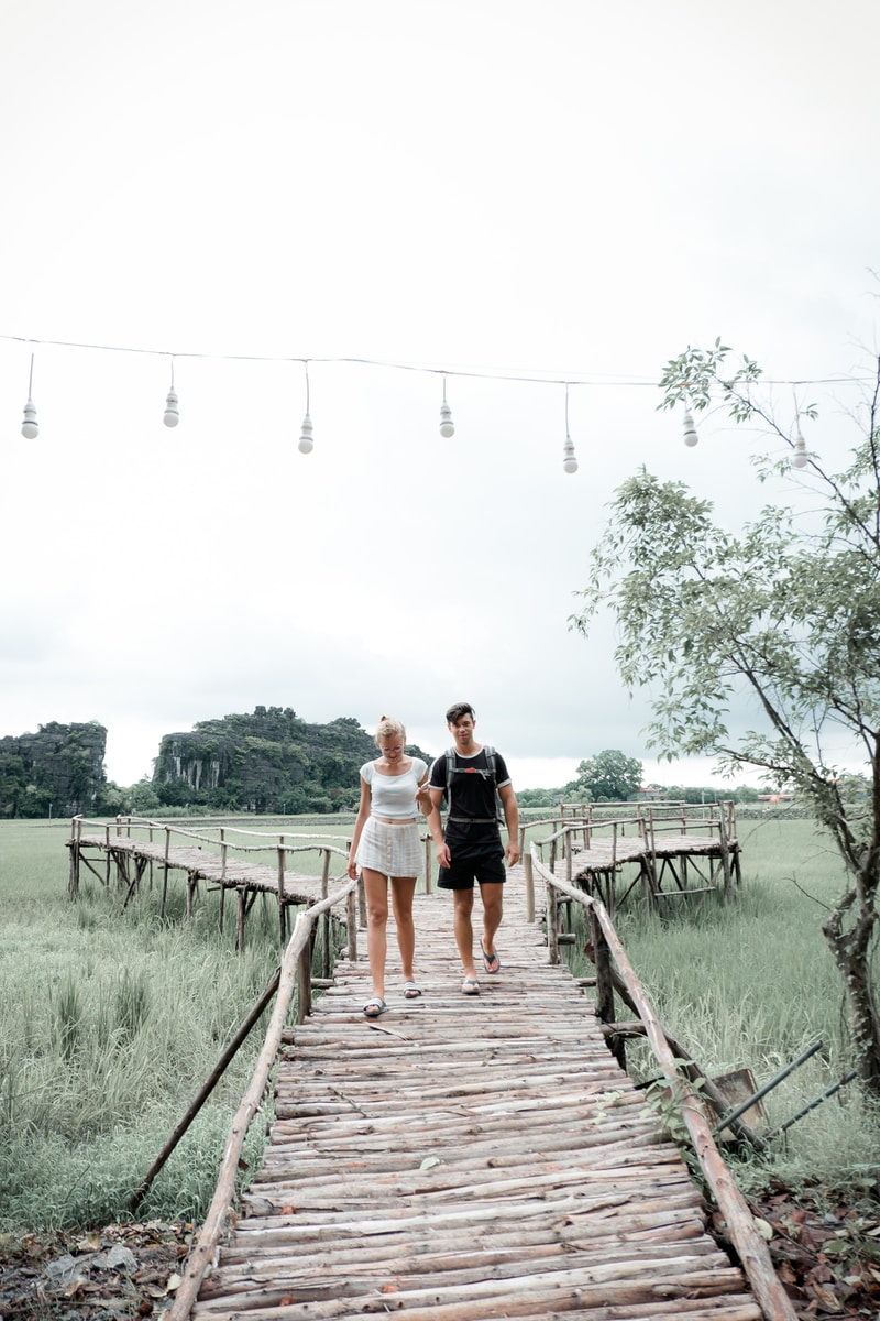 man and woman walking on brown wooden bridge